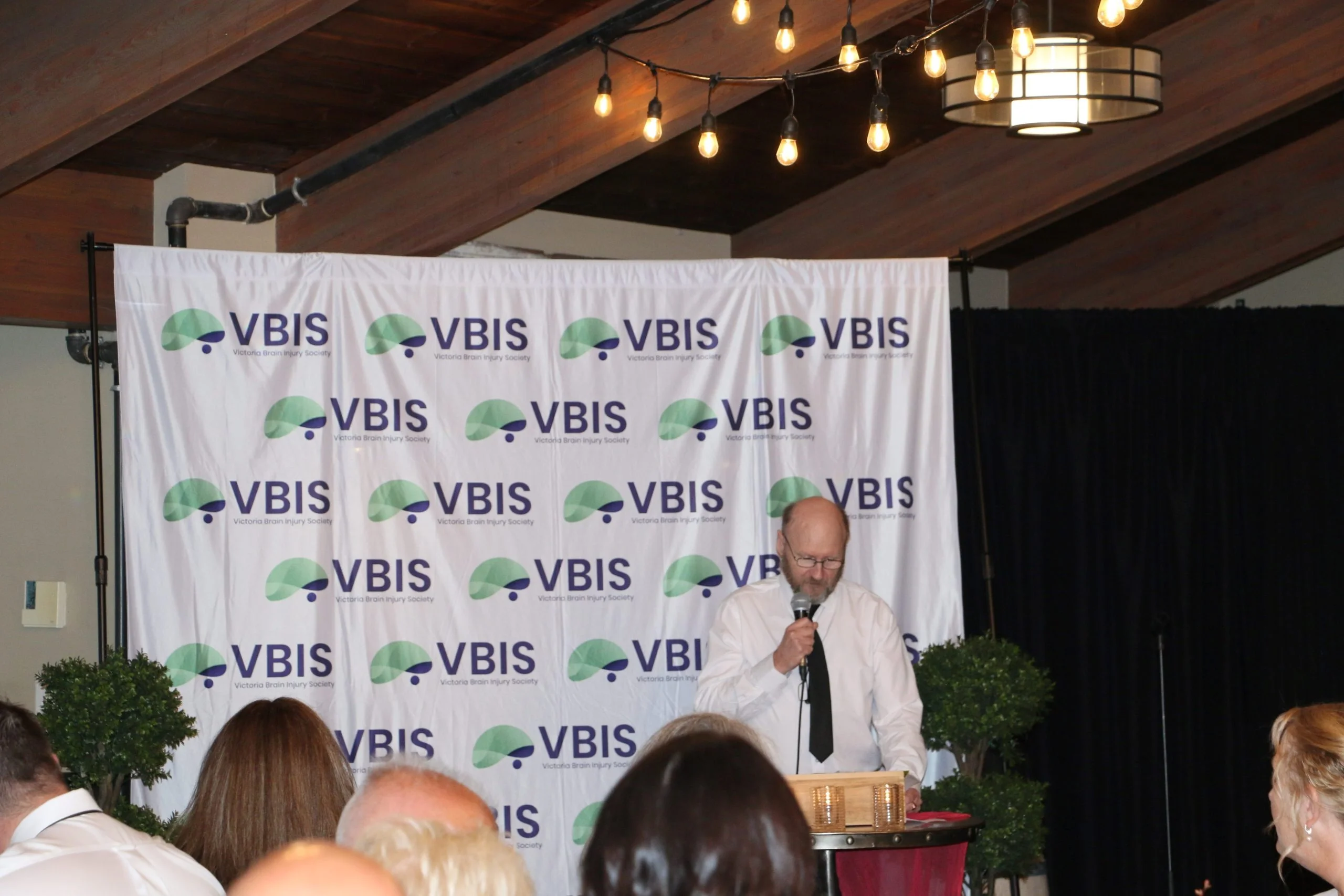 A person at podium giving a speech to a group of people about the Victoria brain injury society